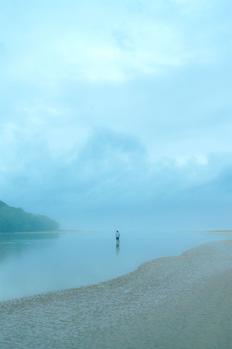 Landscape photography — lone figure standing in still water under a misty blue sky