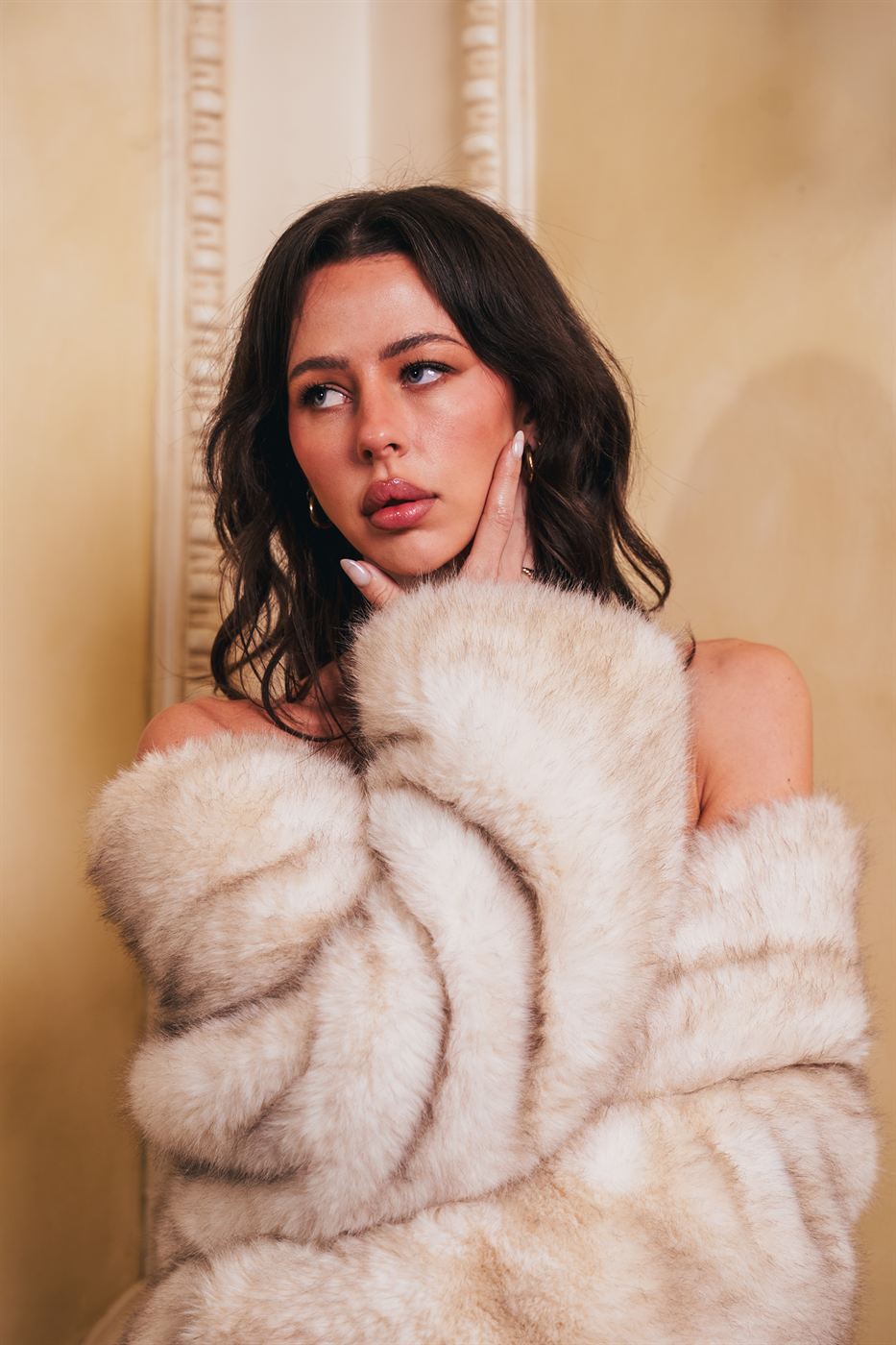 Editorial portrait — model in a cream faux fur coat against an ornate wall